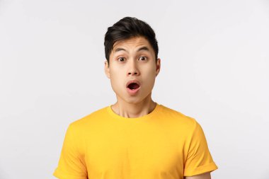 Yakın çekim şaşkın, etkilenmiş ya da şaşırmış Asyalı bir adam, bir şey yakaladı ve kameraya huşu ile baktı, vay canına, çene aşağı ve nefes nefese, sarı tişört içinde beyaz arka plan üzerinde merak