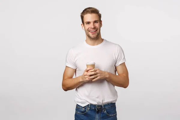 Lifestyle, technologie en stedelijk concept. Knappe glimlachende blonde man met een papieren kop koffie, bestel afhaalmaaltijden, luister muziek in draadloze oortelefoons, gebruik een koptelefoon om vriend te spreken via handen bezig — Stockfoto