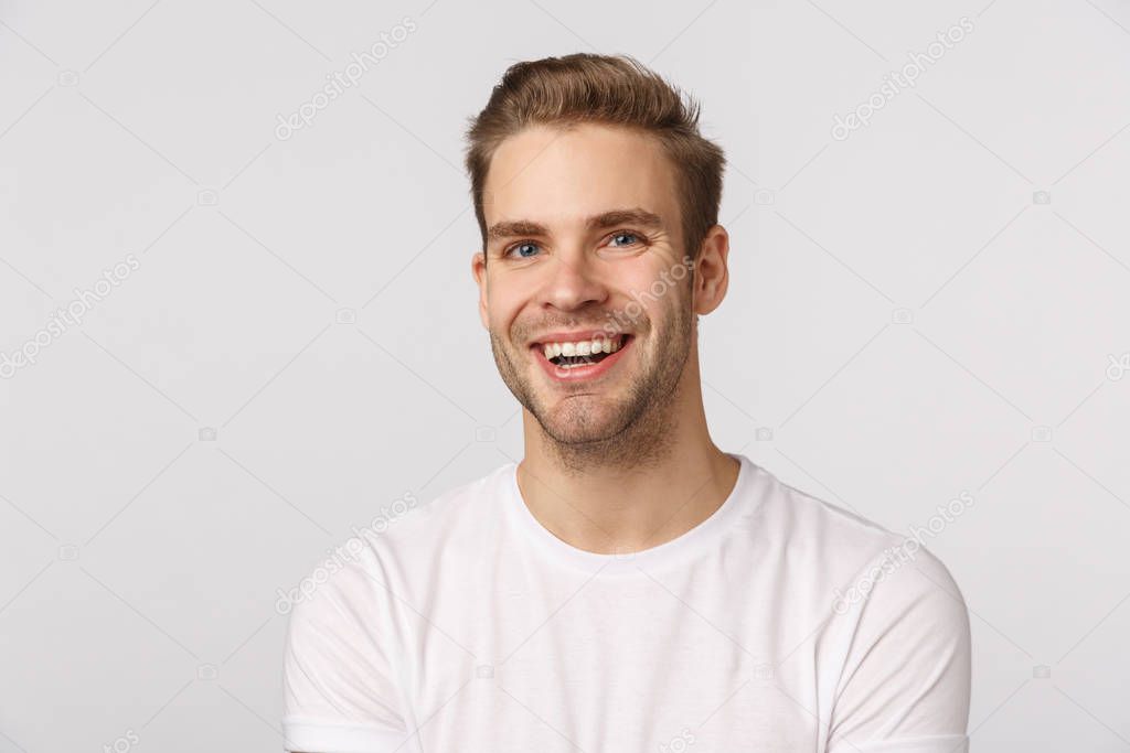 Dreamy charming blond caucasian guy with blue eyes and bristle, laughing and smiling from happiness and delight, express positive emotions, look cheerfully and upbeat, white background