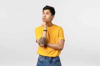 Düşünceli, yakışıklı, dövmeli Asyalı bir erkek arkadaş. Düşünceli bir duruş takınıyor, çeneye dokunuyor, önemli kararları düşünüyor, çözüm düşünüyor, fikir üretiyor, kaş çatıyor.