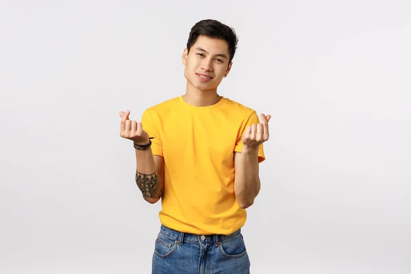 Elegante, bello e fiducioso giovane asiatico hipster in t-shirt gialla con tatuaggi, mostrando due gesti del cuore coreano e sorridente sciocco, esprimere affetto, emozioni positive e gioia — Foto Stock