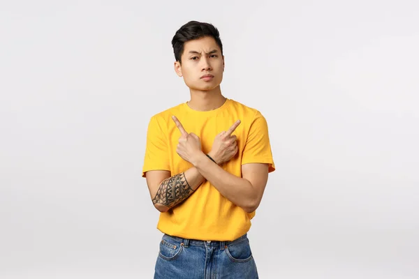 Perplexed and hesitant skeptical asian male customer, facing hard choice, difficult decision during promo, sale offer, pointing sideways with arms crossed over chest, showing left and right variant — Stock Photo, Image