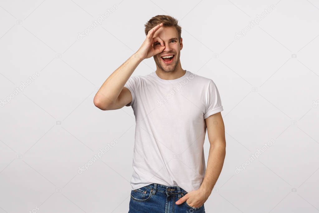 Happy cheerful blond male model with bristle, wear white t-shirt, looking through circle or okay sign with satisfied smile, leave positive feedback, give approval, like product, white background