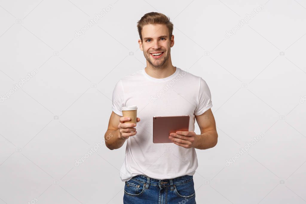 Business, work and lifestyle concept. Modern good-looking blond caucasian guy having break, drink coffee from paper cup, holding digital tablet, look camera, talking casually during office lunch