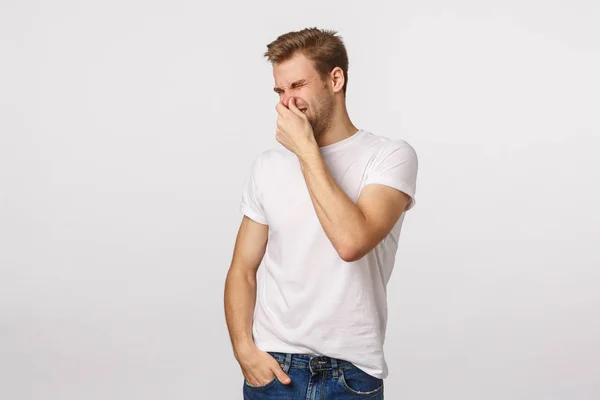 Gosh whats that smell. Disgusted and reluctant blond bachelor man open fridge and close nose with hand, squinting turn away from disgust, something reek, stink, standing white background — Stock Photo, Image