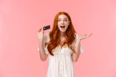 Belden yukarı portre eğlendi, şaşırdı ve heyecanlı modaya uygun kızıl saçlı kız bankada büyük tanıtımlar ve ikramiyeler hakkında konuştu, kredi kartı tuttu ve şaşkın, pembe arka plan