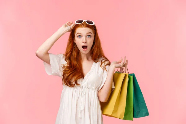 Waist-up portrait impressed, excited and surprised ginger girl, foxy curly hair, take-off sunglasses, seeing amazing discounts in store, hurry up to buy something, holding bags with shopping goods — Stock Photo, Image