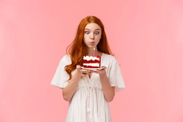 Believe in miracle. Cute and silly wishful redhead girl making wish on birthday, blowing out candle on b-day cake with focused expression, having fun, partying and celebrating in family circle — Stock Photo, Image