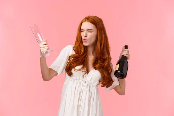 Мбаппе, вечеринка и веселая концепция. Пьяная и беззаботная, взволнованная рыжая женщина, стоящая впустую, чувствующая головокружение и оптимизм, держащая бутылку шампанского и бокал, похмелье рядом — стоковое фото