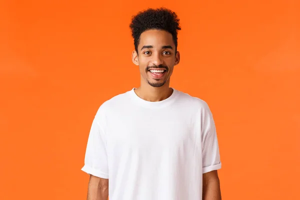 Veselý mladý hipster africký Američan s knírem a afro účesem, oblečený v bílém tričku, usmívající se roztomilá kamera šťastná, stojící oranžové pozadí expresivní pozitivita — Stock fotografie