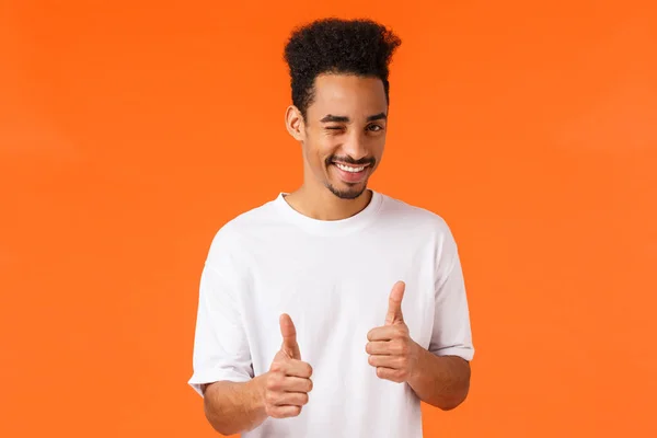 Tu consegues, diz que sim. Alegre e confiante jovem homem africano-americano de apoio em t-shirt branca, piscadela e sorriso, mostrando gesto polegar-up, enraizamento, incentivar tudo bom, bom trabalho — Fotografia de Stock