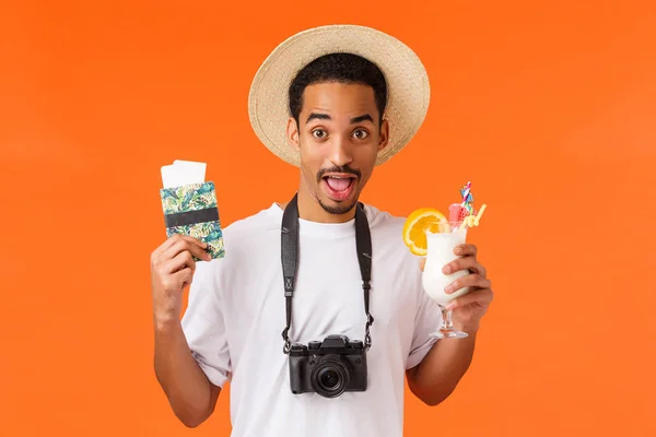 카메라와 모자를 착용하고 따뜻 한 시골 휴가를 즐기고 있는 아프리카 계 미국인 남성인 앰무는 여권 과 칵테일, 오렌지 배경을 가진 채 휴일 리조트에 갔다. — 스톡 사진