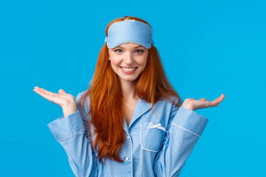 Who knows, dont care. Carefree and unbothered happy smiling redhead female in nightwear, sleep mask, shrugging indecisive and clueless with hands raised sideways, standing blue background clipart
