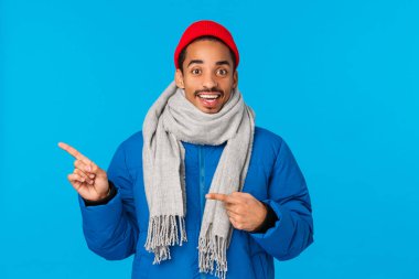 Neşeli ve mutlu, neşeli, gülümseyen Afro-Amerikalı bir adam harika bir bayram etkinliği gösteriyor, havalı reklam bilgileri veriyor, sol davetlileri işaret ediyor, kışlık giysiler giyiyor.