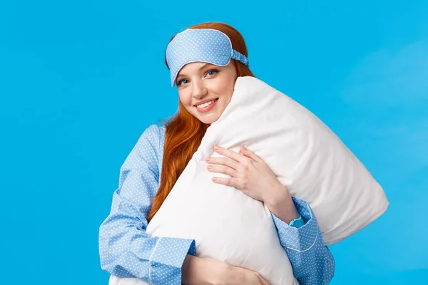 Sleepy time. Lovely and feminine glamour redhead girl with sleep mask, wearing nightwear, hugging pillow and smiling, wishing sweet dreams, standing blue background upbeat — Stock Photo, Image