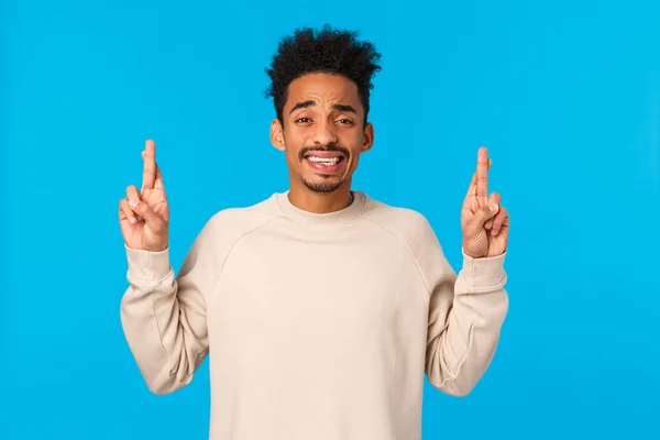 Nervous timid and cute african-american guy with afro haircut scared telling parents something huge, pointing fingers up, cringe and smiling with anxious expression, feeling alarmed, blue background — Stock Photo, Image