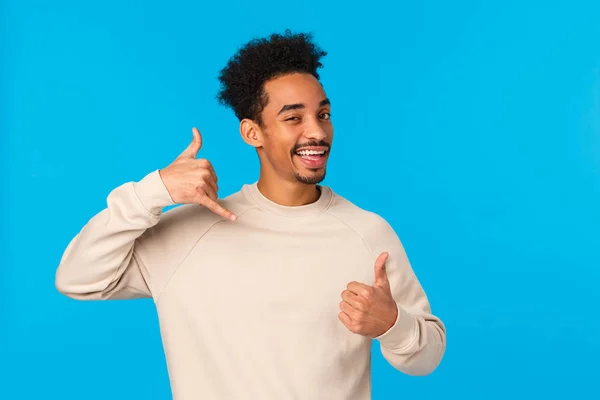 Chiamami dopo, tesoro. Sassy e civettuola afro-americano fiducioso macho ragazzo con i baffi, taglio di capelli afro mostrando pollice in su e gesto del telefono, occhiolino e sorridente flirty, sfondo blu — Foto Stock