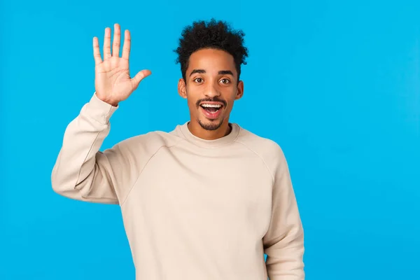 People, communication and chatting concept. Happy outgoing smiling nice african american guy with moustache and afro haircut meeting new friends, saying hi wave hand in hello gesture, blue background — 스톡 사진