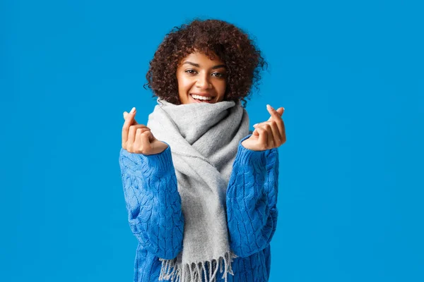 Romântico e bobo bonito namorada afro-americana, corte de cabelo afro, camisola de inverno e cachecol, esperando dia dos namorados presente e data, mostrando sinais de coração coreano e sorrindo, fundo azul — Fotografia de Stock