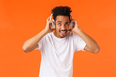 Komşuların iğrenç müzik zevkine ve gürültüsüne katlanamıyor. Kulaklıklarını takıp en sevdiği şarkıları söylüyor. Çalma listesini dinliyor, rahatsız ve tatminsiz turuncu arka plana bakıyor.