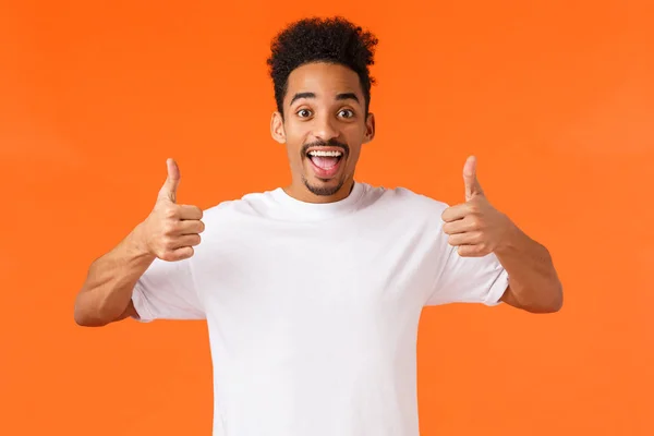 Amused and excited happy african-american guy showing thumbs-up and agrees with friend travel abroad summer vacation, like idea, approve something great, standing orange background — Stock Photo, Image