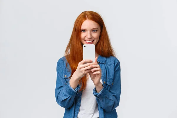 Amistad, unión y concepto de estilo de vida moderno. Linda chica pelirroja en busca de ángulo perfecto, tomando fotos de un amigo en el teléfono inteligente, fogotafing, disparando algo interesante — Foto de Stock