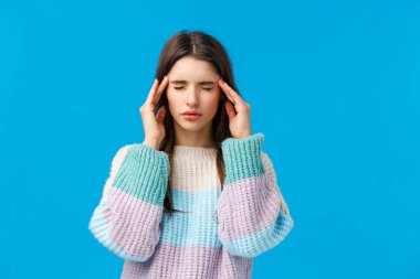 Akşamdan kalma, sağlık ve insan konsepti. Stresli genç bir kadın baş ağrısı çekiyor, gözleri kapalı tapınaklara dokunuyor, ilaçla kolay bir acı çekmeye çalışıyor, migren ağrısı çekiyor, mavi arka planda duruyor.