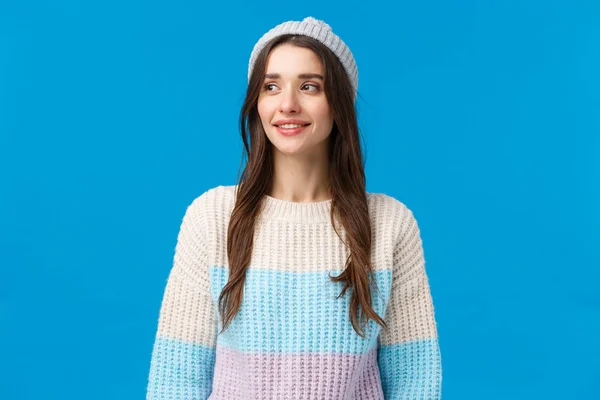Paist-up portret ciekawy szczęśliwy cute girl w czapce zimowej, sweter rozgląda się wokół czekając na przyjaciela grać śnieżki, korzystając z wakacji, uśmiechając się szeroko, stojąc niebieskie tło entuzjastyczne — Zdjęcie stockowe