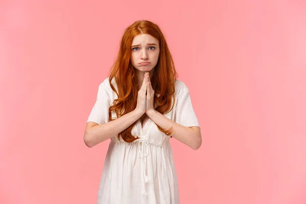 Sombres et tristes, mignonne rousse boudeuse demandant de l'aide, regardant appareil photo plein d'espoir, faire des promesses ou des excuses, serrer les mains ensemble dans la prière, mendier faveur, plaidoyer sur fond rose — Photo