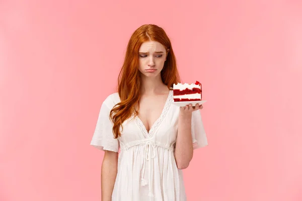伤心、不安和沮丧的红头发女孩感到孤独或伤心，吃东西时不要想坏主意，拿着和平蛋糕，看着甜食时很伤心，叹着气 — 图库照片