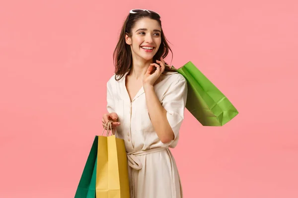 Nyugodt és gondtalan csillogás, nőies aranyos lány ruha gazdaság bevásárló táskák és jobbra fordult gyönyörű boldog mosollyal, élvezi bolt divatos üzletek, álló rózsaszín háttér — Stock Fotó
