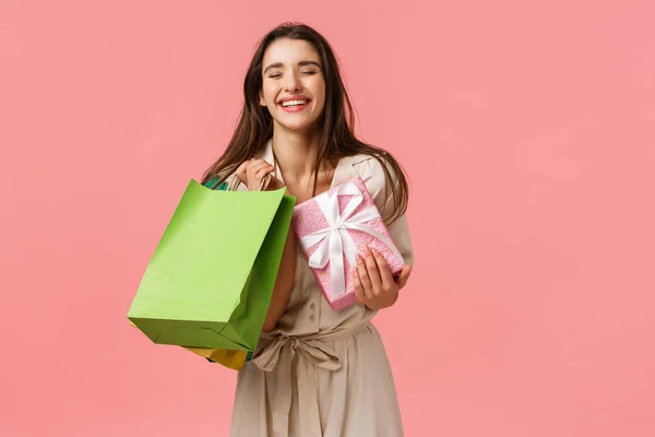 Щастя, подарунки та концепція святкування. Весела щаслива і безтурботна дівчина, яка насолоджується покупками, має гарний денний магазин, тримає сумки і подарунки в магазині, очі сміються збудженим, рожевим фоном — стокове фото