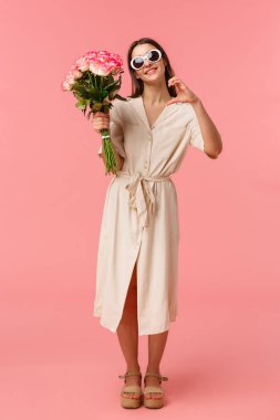 Tam boy dikey portre romantik ve şehvetli genç bir kadın elinde buket çiçekleri tutarak kalp işareti yapıyor. Sevgisini ifade ediyor ve güllerle şükran duyuyor.