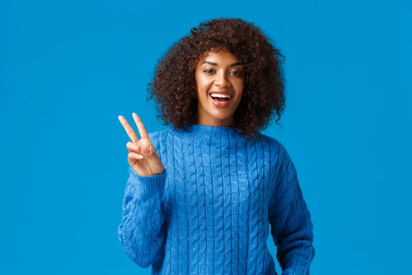 Feliz año nuevo y paz. Alegre chica hipster afroamericana relajada y despreocupada con corte de pelo afro en suéter de invierno, mostrando gesto de victoria y sonriendo, deseando a todos lo mejor — Foto de Stock
