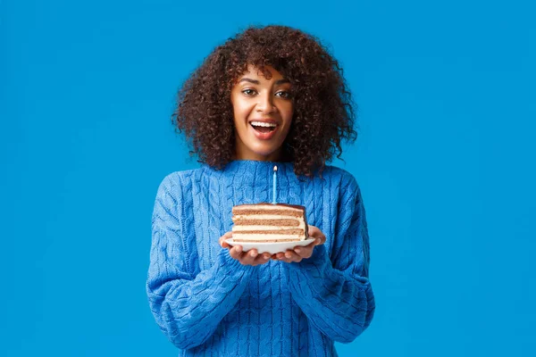 Pide un deseo y se hará realidad. Alegre y soñadora linda africana-americana b-day girl, celebración de pastel con vela, soplado y sonriente, teniendo fiesta de cumpleaños, de pie en suéter fondo azul — Foto de Stock