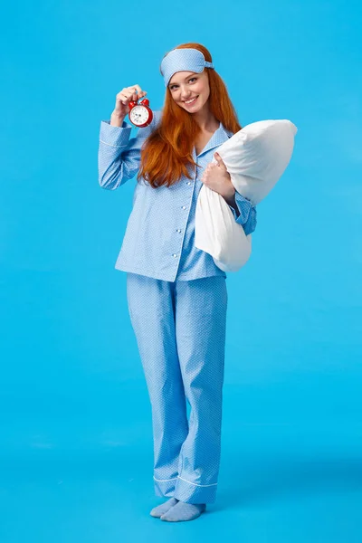 Wanna go bed. Pretty coquettish and silly european feminine redhead teenage girl with red alarm clock holding pillow, wearing pyjama and sleep mask, going have sweet dreams, smiling camera — Stock Photo, Image