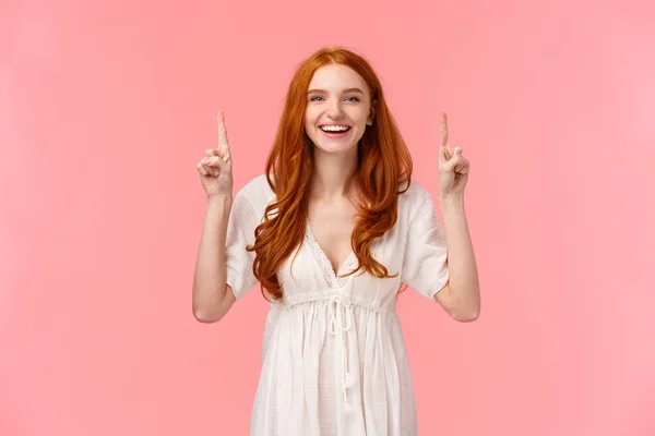 Feliz sorrindo ruiva fêmea europeia no elegante vestido branco, apontando os dedos para cima rindo da câmera, publicidade promo, mostrando banner da empresa, produto de beleza favorito — Fotografia de Stock