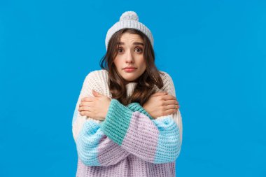 Süveter ve kışlık şapkalı aptal, çekingen, çekingen, çekingen, esmer kız. Soğuk havadan sallanarak vücut ısısını kucaklıyor. Masum bir kameraya bakıp, ısıtıcıyı açmasını istiyor.