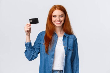 Banka, finans ve eğitim konsepti. Neşeli, yarı zamanlı çalışan, ilk maaş çekini alan, elinde kredi kartı tutan, kendine güvenen, ayakta duran, beyaz bir geçmişi olan, mutlu bir kız.