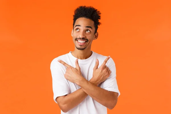 Nadšený, vzrušený afroameričan s knírkem, vzhlíží zasněný a bezstarostný, šťastně se usmívá, ukazuje bokem doleva a doprava, dělá rozhodnutí, co koupit, oranžové pozadí — Stock fotografie