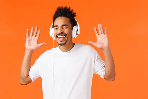 Fantastica qualità del suono. Felice spensierato, sorridente uomo afro-americano in t-shirt bianca che canta e fa gesti come godendo della musica preferita, ascolta la traccia in cuffia, chiudi gli occhi e sorridi felice — Foto Stock