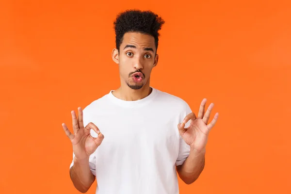 Guy Rating gibt Feedbak über nicht schlechten Film. Netter Hipster moderner afrikanisch-amerikanischer Mann in weißem T-Shirt drückt persönliche Meinung aus, zeigt okay, gute Geste, orangefarbener Hintergrund — Stockfoto