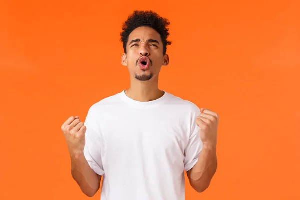 Aliviado e animado triunfante afro-americano cara sentindo-se feliz alcançar o sucesso, ganhar se tornar campeão, bomba de punho gritando sim e olhando céu satisfeito, fundo laranja — Fotografia de Stock