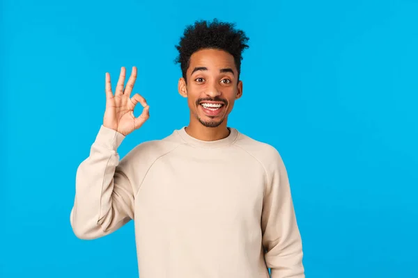 Wesoły szczęśliwy uśmiechnięty Afroamerykanin z hipsterską fryzurą, pokazując w porządku gest i kiwnij głową w porozumieniu, dać aprobatę, potwierdzić lub zgodzić się uczestniczyć, stojąc niebieskie tło zadowolony — Zdjęcie stockowe