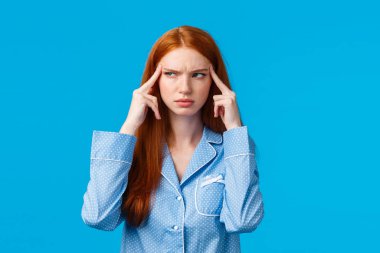 GIrl trying focus and think straight. Serious-looking thoughtful redhead creative woman squinting suspicious and hesitant, touching temple look away with disbelief, thinking, blue background clipart
