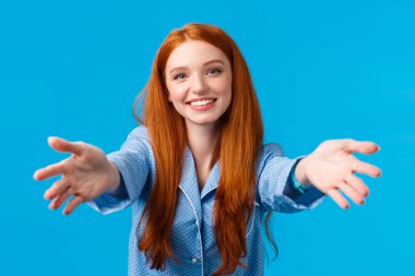 Seni kollarıma almama izin ver. Şefkatli ve kadınsı kızıl saçlı kadın, yastık ve uykuyu kucaklamak için ellerini uzatıyor, neşeli bir ifadeyle gülümsüyor, pijama giyiyor, mavi duvar