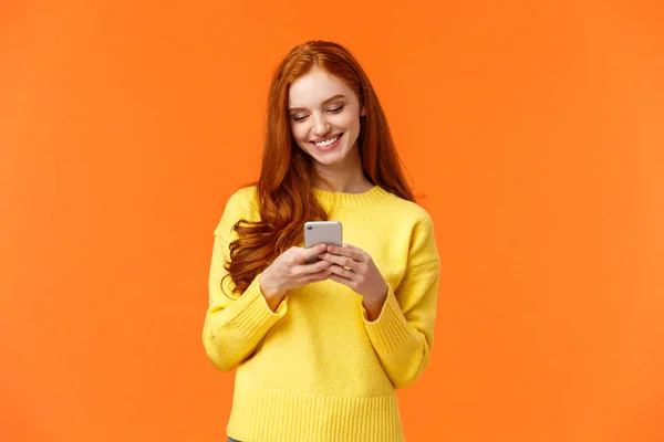 Comunicación, gente y concepto de chat. Despreocupado chica hipster moderna editar fotos con filtros en la aplicación de teléfono inteligente, aplicación de uso para chatear, sonriendo como pantalla móvil que mira, fondo naranja — Foto de Stock