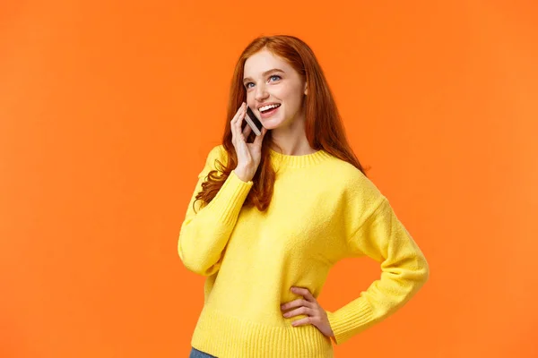 Chica pelirroja bonita saliente conversando por teléfono, llamando a un amigo, haciendo arreglos, reservando hotel o viaje con el móvil, hablando por teléfono inteligente, de pie fondo naranja — Foto de Stock