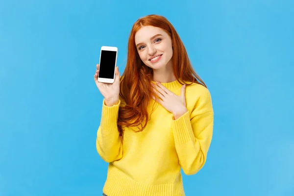 Touched lovely and romantic redhead cute woman bragging with photos from winter holidays, showing smartphone display, touch heart and sighing grateful or pleased, blue background — Stock Photo, Image