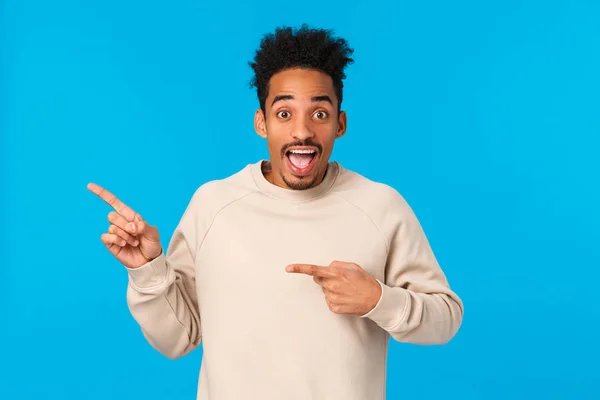 Happy and enthusiastic, excited african-american hipster guy with moustache, afro haircut inviting check this out, pointing upper left corner, telling about party or event, promoting, blue background — Stock Photo, Image